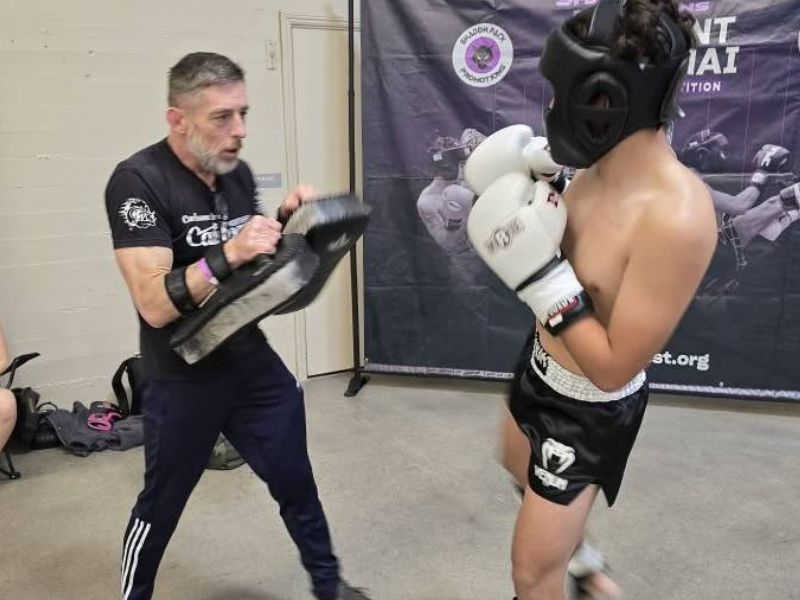 Instructor holding kickboxing pads while coaching a young student